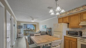 Cozinha compacta com armários de madeira, micro-ondas, geladeira e área de refeições com mesa e cadeiras de madeira.