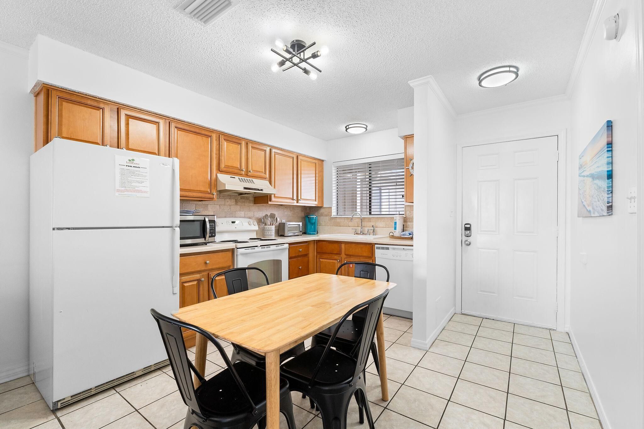 A compact kitchen with wooden cabinets, a white refrigerator, a microwave, and a stove. There is a dining table with four chairs.