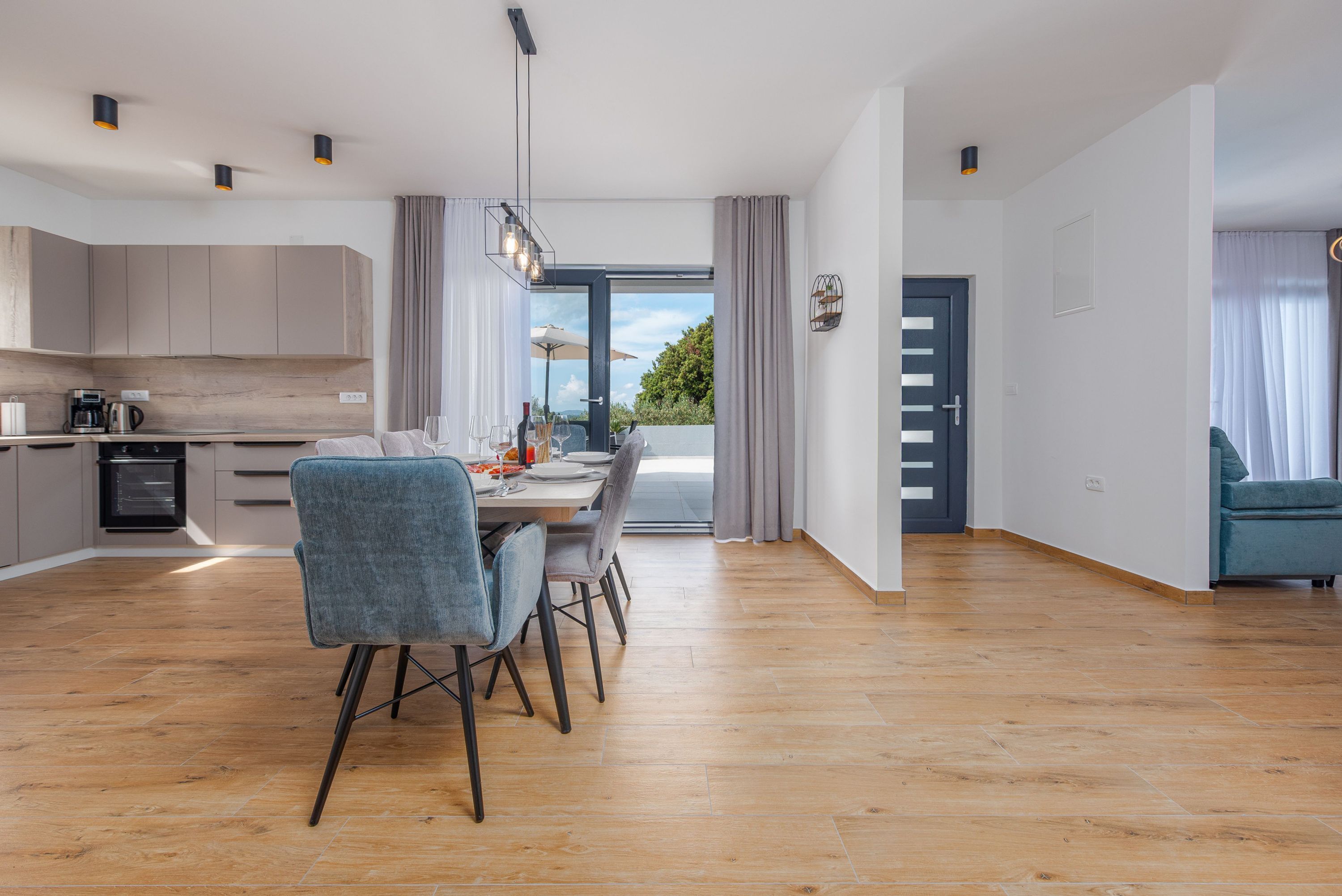 Una cocina moderna con armarios de madera, un comedor con mesa y sillas, y vistas al exterior a través de amplios ventanales.