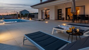 A rooftop pool area with lounge chairs and a table with drinks, surrounded by a building with a tiled roof. - Villa Miki Zadarvillas (Polaca)