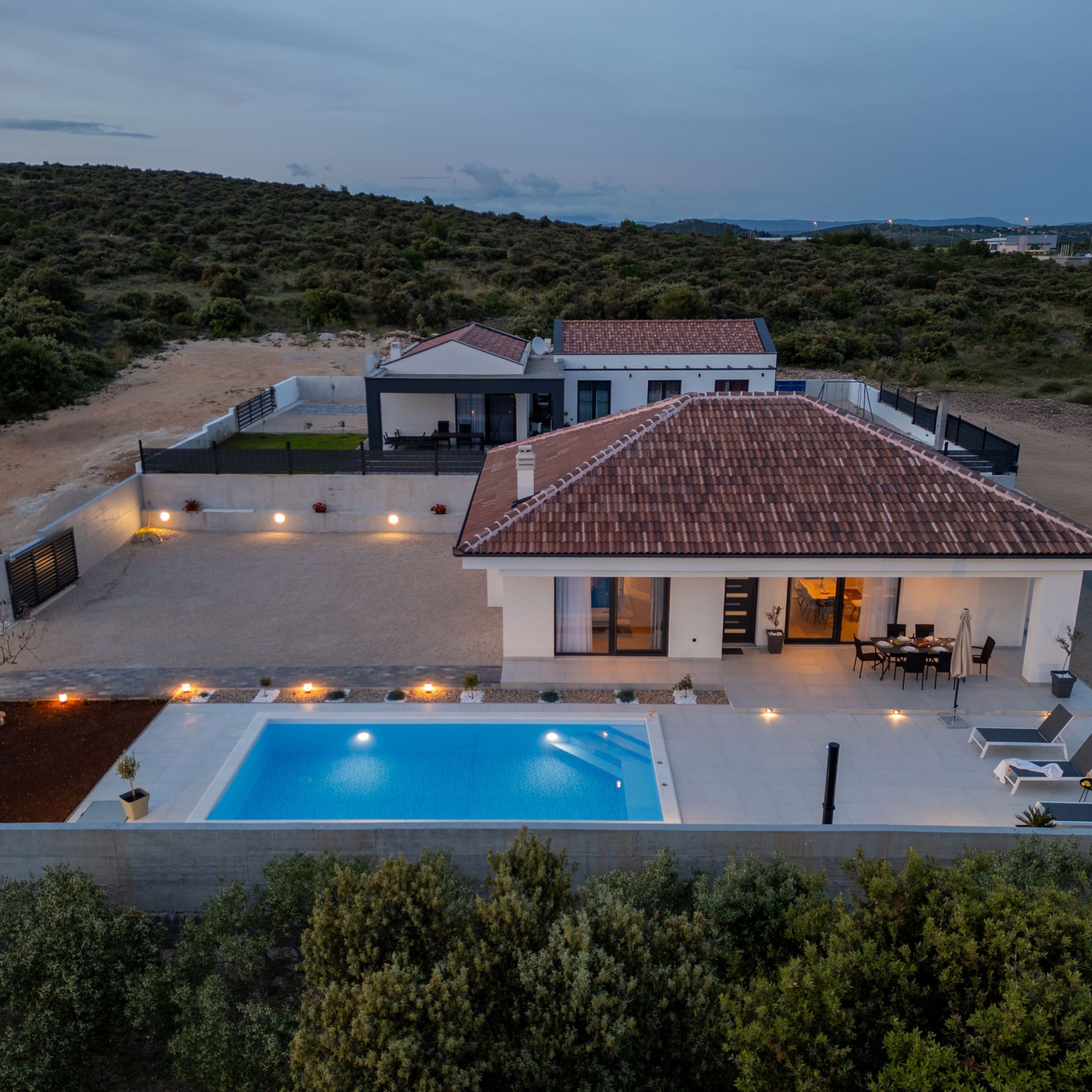 A modern two-story house with a swimming pool, outdoor seating, and a view of the surrounding landscape.