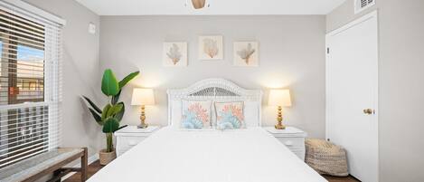 Un dormitorio con cama, ventilador de techo, lámparas de noche, decoración en la pared y una planta en maceta.