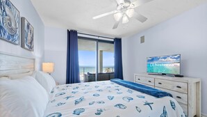 A bedroom with a bed, a television, a ceiling fan, and a window with curtains. - Pelican Pointe 506 (Orange Beach)