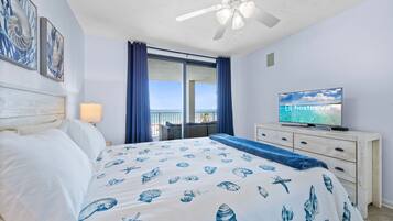 A bedroom with a bed, a television, a ceiling fan, and a window with curtains.