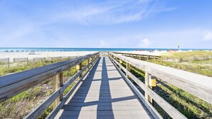 A wooden boardwalk leading to a beach with a clear sky. - Pelican Pointe 506 (Orange Beach)