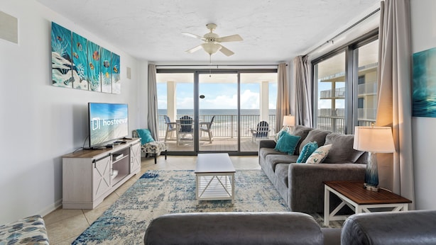 A living room with a TV, sofa, and a balcony with a view. - Pelican Pointe 506 (Orange Beach)
