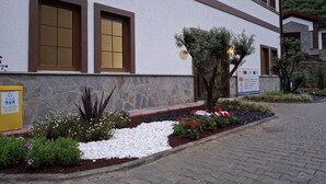 A building with a stone facade, two large windows with brown frames, and a small tree in the front garden. - Çardak Alti Otel (Arsin)