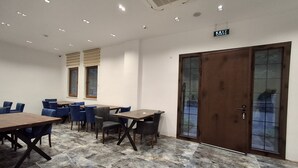 A conference room with marble flooring, blue chairs, wooden tables, and a large wooden door with glass panels. - Çardak Alti Otel (Arsin)