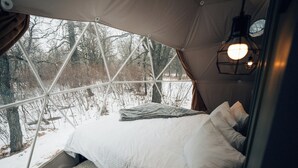 A cozy bed with a view of a snowy forest through a large window. - Oak Haven Oasis ~ Dome 1 (Brandon)