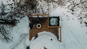 A snow-covered outdoor area with a wooden deck, a hot tub, and a spherical structure with a star-shaped window. - Oak Haven Oasis ~ Dome 1 (Brandon)