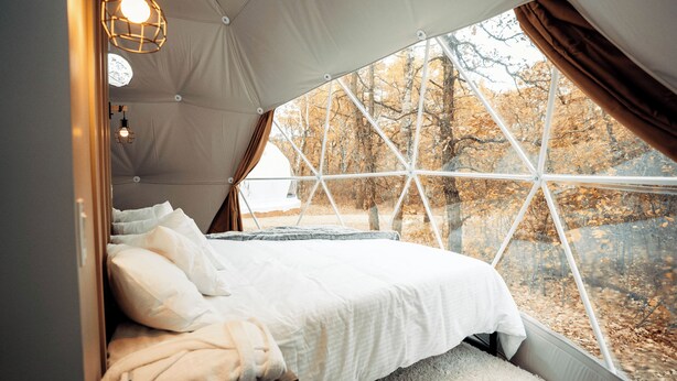 A tented accommodation with a bed, white bedding, and a view of trees through a large window. - Oak Haven Oasis ~ Dome 3 (Brandon)