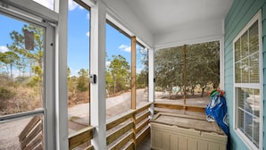 A covered porch with a wooden bench, a radiator, and a view of trees and a road. - The Rookery 3504 (Gulf Shores)