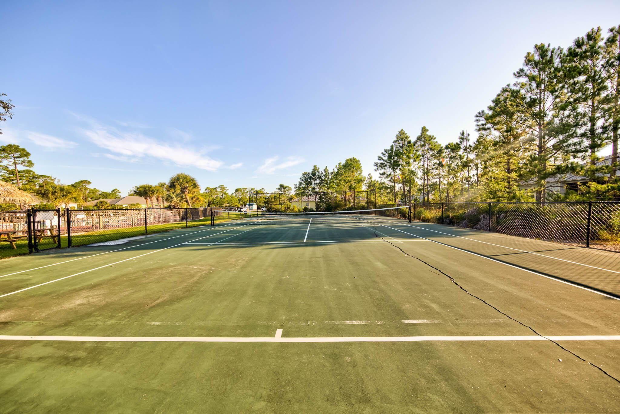 An outdoor tennis court with a net, surrounded by trees and a fence.