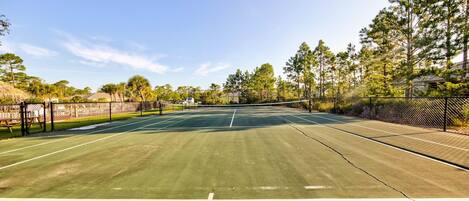 An outdoor tennis court with a net, surrounded by trees and a fence.