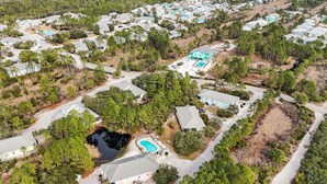An aerial view of a residential area with multiple houses, a swimming pool, and a large body of water. - The Rookery 3504 (Gulf Shores)