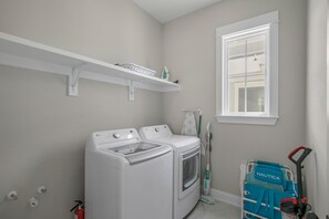 A laundry room with two white washers and dryers, a window, a shelf with laundry supplies, and a blue cart labeled "NAUTICA". - Summer Salt 24170 (Orange Beach)