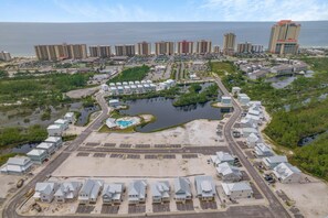 An aerial view of a coastal resort with multiple buildings, a central pool area, and surrounding greenery.