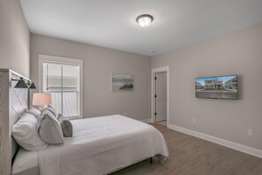A bedroom with a bed, a window with blinds, a door, and a wall-mounted picture.