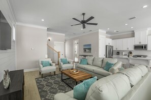 A modern living room with a sofa, coffee table, and a TV. There is a staircase leading to another room.