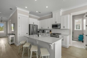 A modern kitchen with white cabinetry, stainless steel appliances, and a large island with bar stools.