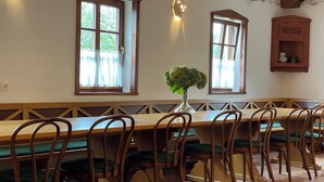 A dining area with a long wooden table and chairs, large windows with curtains, and a vase with greenery. - A cozy and luxurious house with a pool beneath mount Donačka gora. (Rogatec)