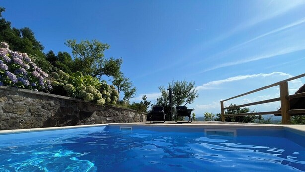 A swimming pool with clear blue water, surrounded by a stone wall and lush greenery. - A cozy and luxurious house with a pool beneath mount Donačka gora. (Rogatec)