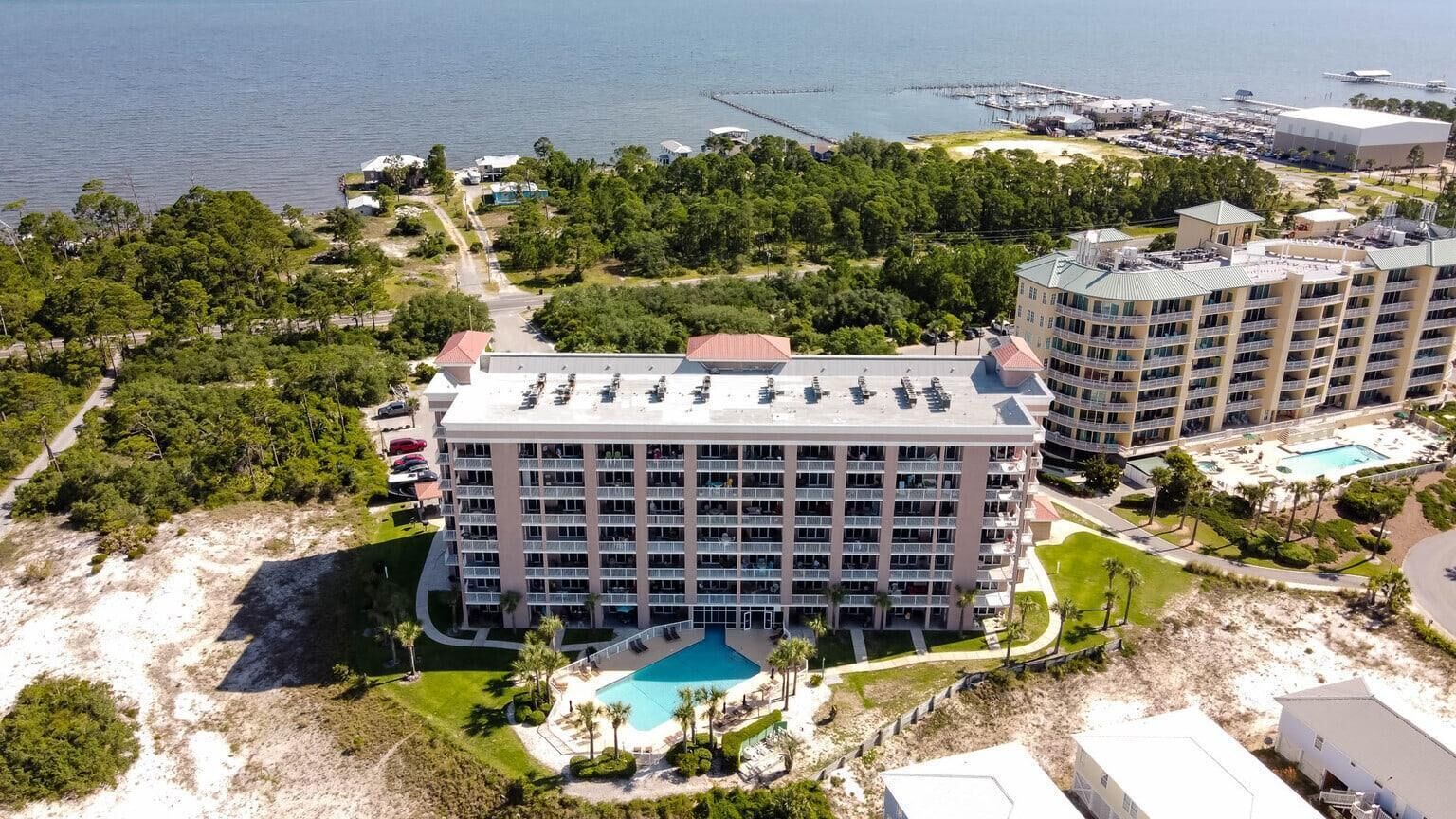 Ein mehrstöckiges Hotel mit Pool, umgeben von viel Grün und einem Strand.