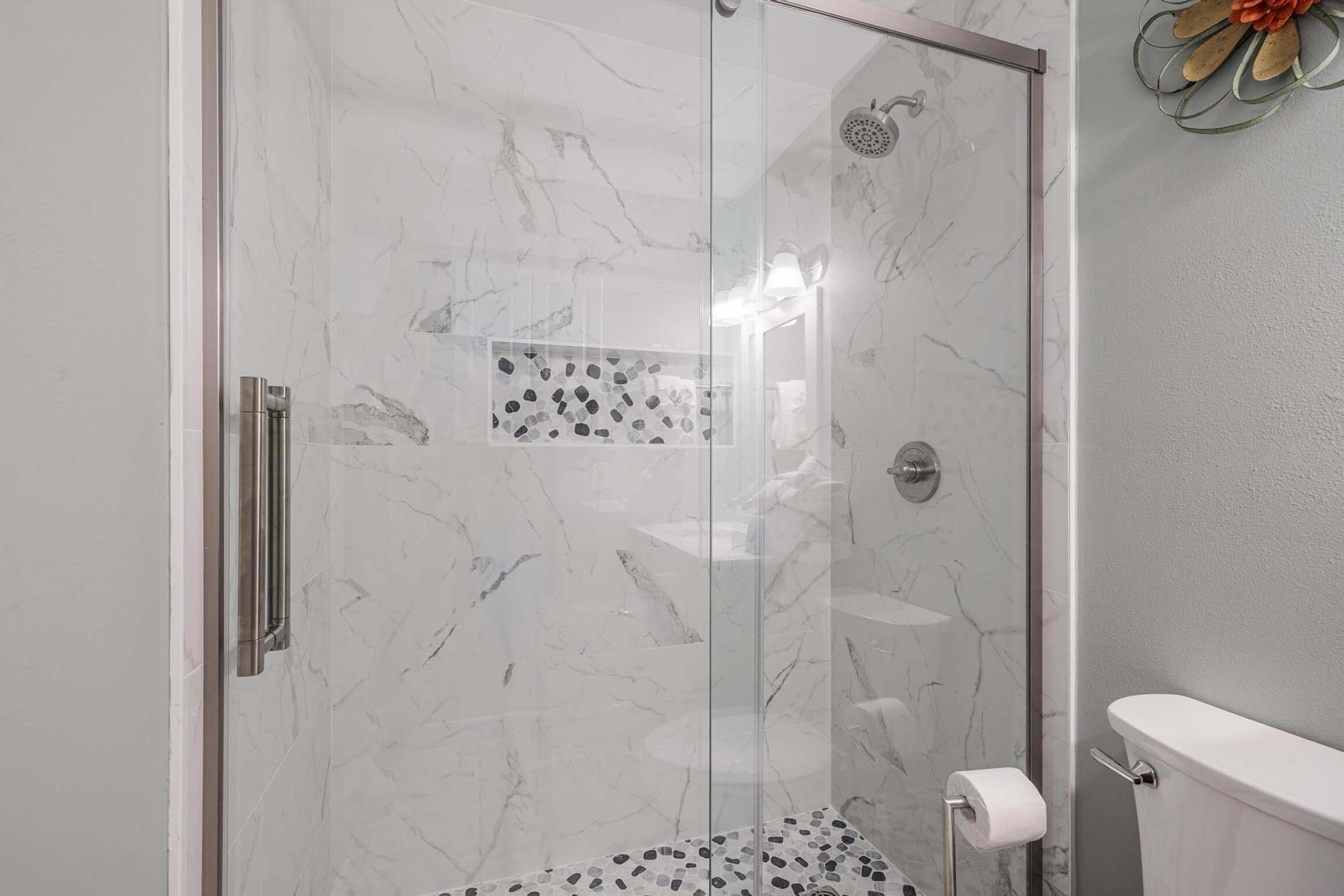 A glass-enclosed shower with a marble floor and a toilet visible to the right.