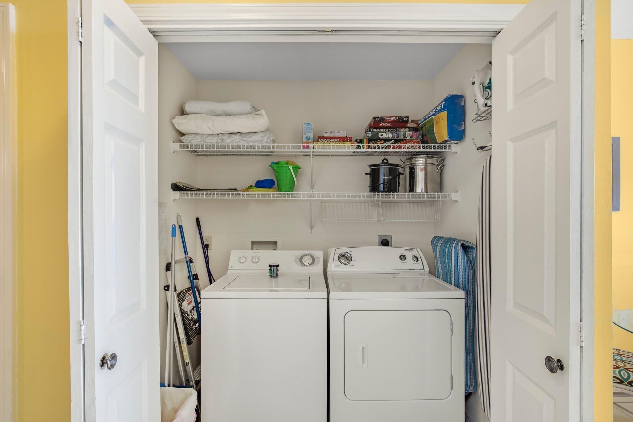 A laundry room with two washing machines, shelves with folded towels, cleaning supplies, and a drying rack.