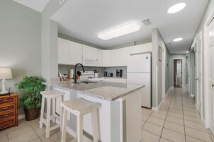 Una cocina moderna con armarios blancos, encimera de granito y una isla central con taburetes.