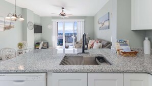 A modern kitchen with granite countertops, a built-in dishwasher, and a large window offering a city view. - The Dunes 502 (Gulf Shores)