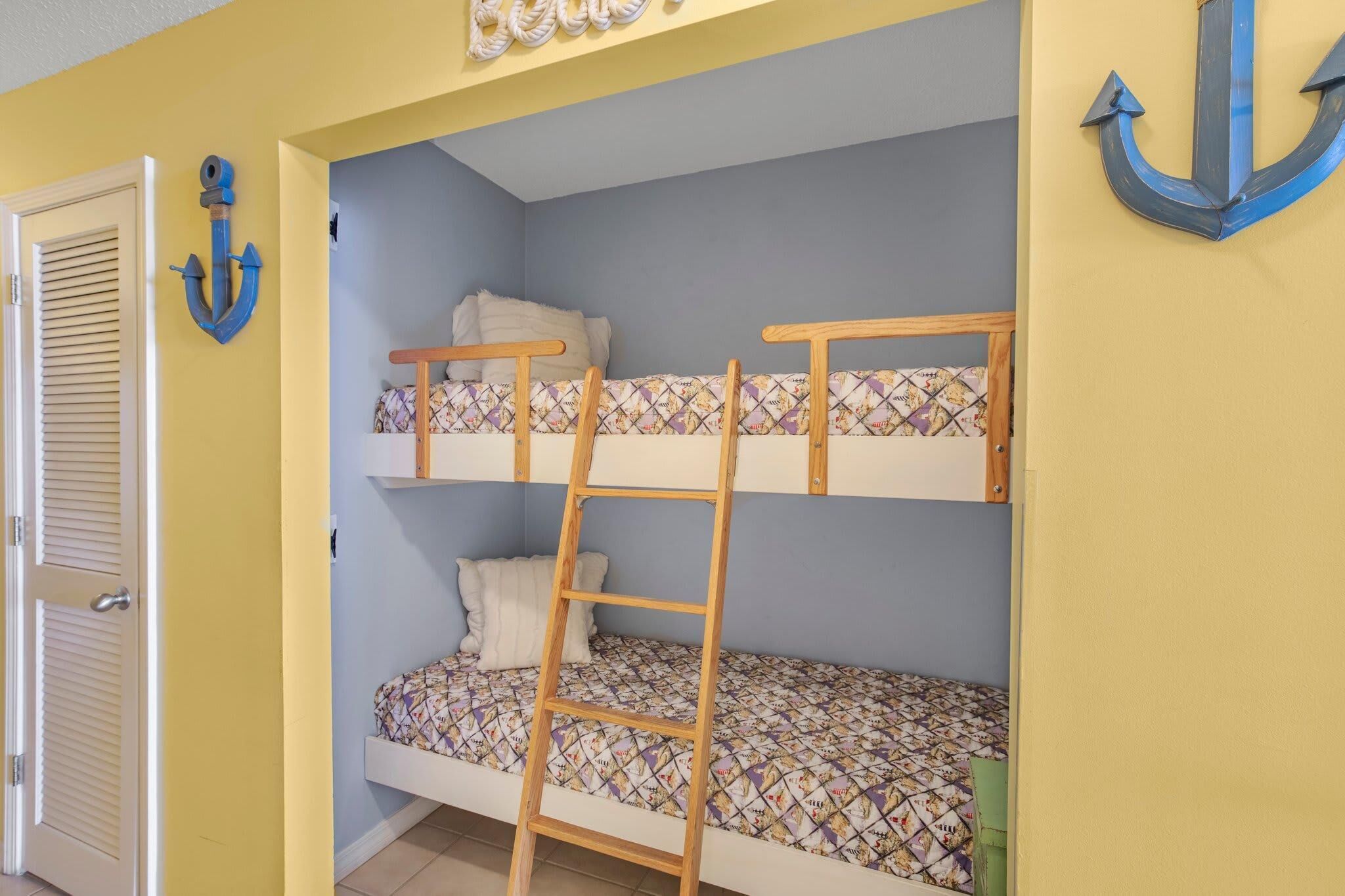 Habitación con literas, una escalera, una puerta y un adorno de ancla en la pared.
