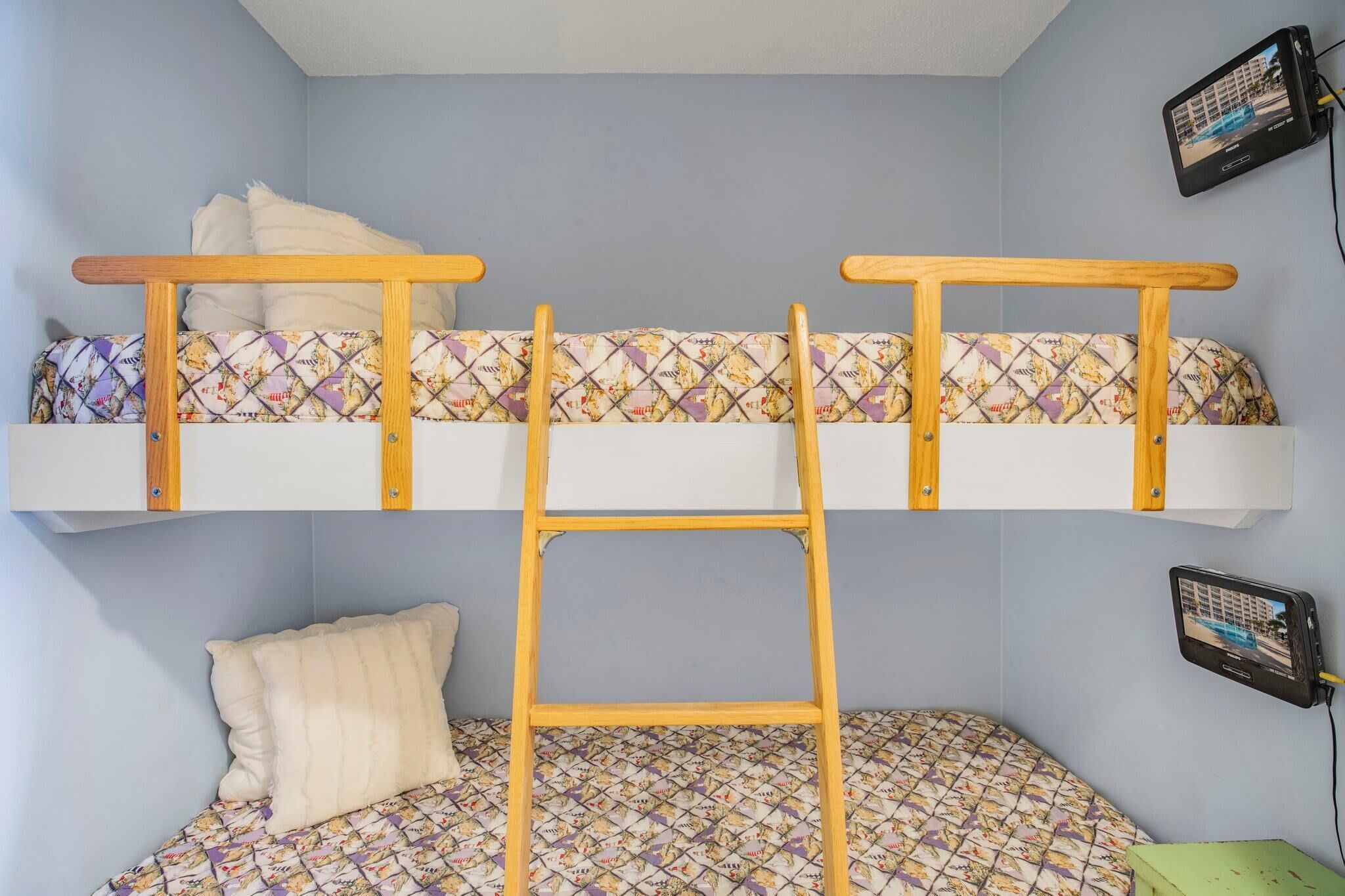 A bunk bed with a ladder, a pillow, and a wall-mounted TV.