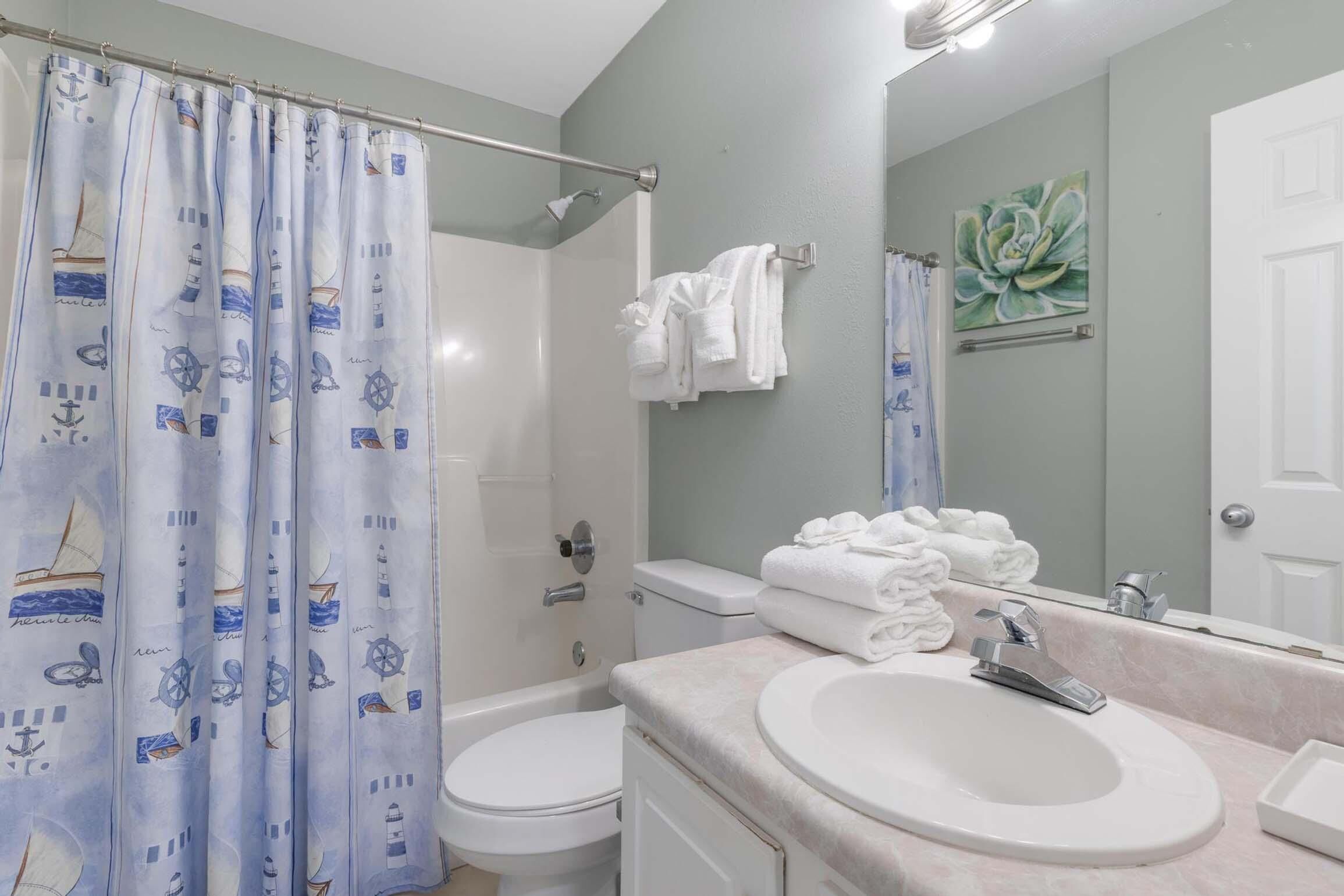 A bathroom with a shower curtain featuring nautical designs, a toilet, a sink with a mirror, and a towel rack with folded towels.