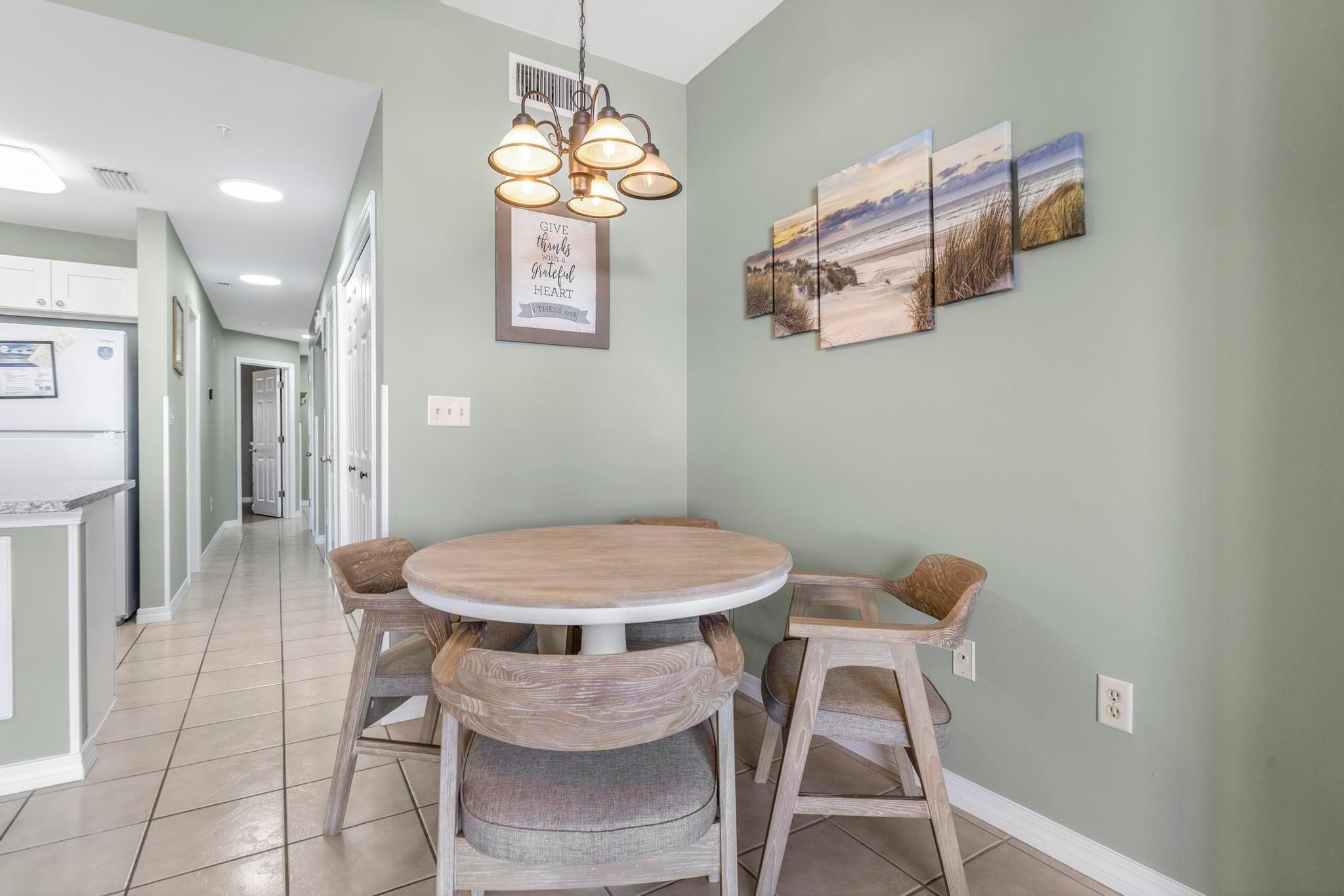 Een eethoek met een ronde tafel, vier houten stoelen, een hanglamp en drie landschapsprenten aan de muur.