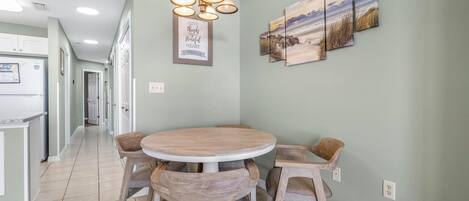 Een eethoek met een ronde tafel, vier houten stoelen, een hanglamp en drie landschapsprenten aan de muur.