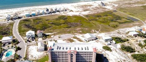 An aerial view of a coastal hotel with multiple buildings, a large parking area, and a beach in the background.