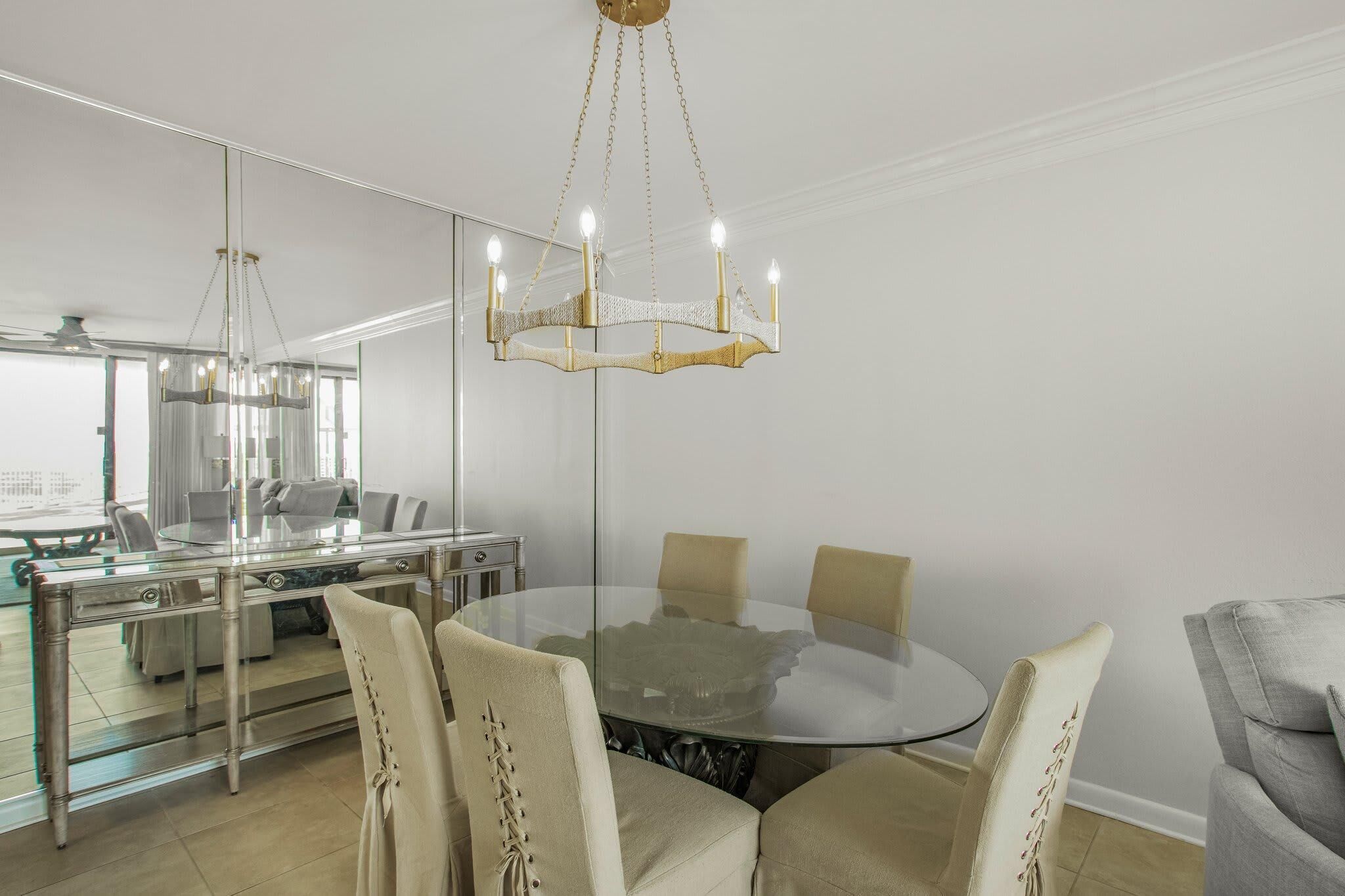 A modern dining area with a glass table, beige chairs, and a chandelier.
