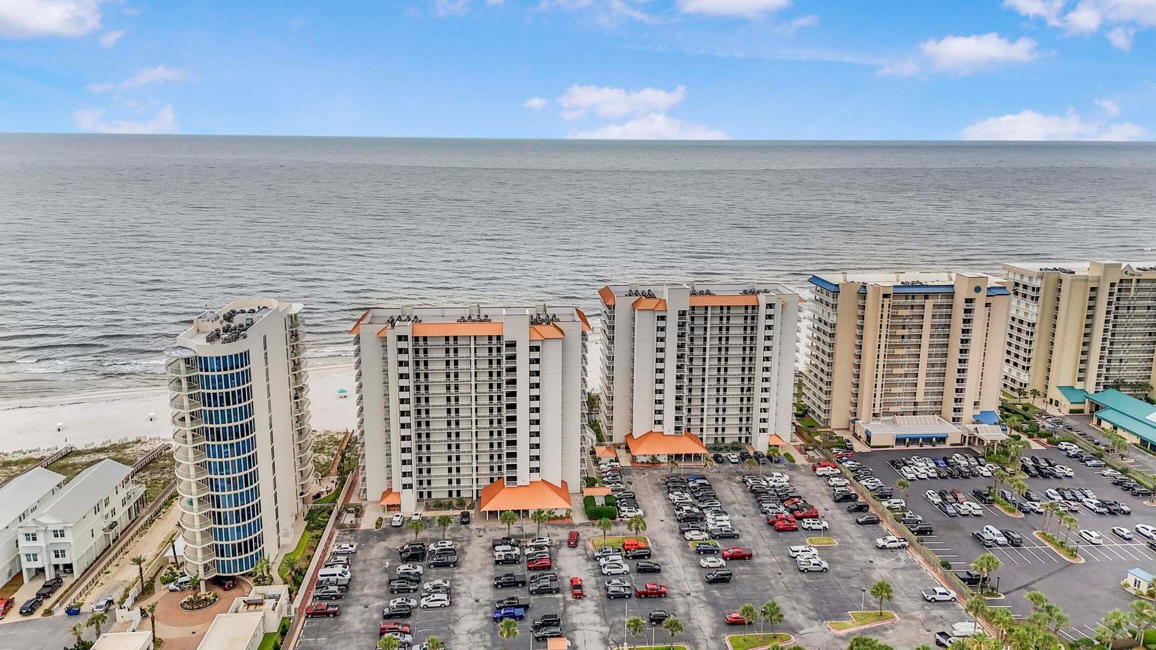 Un hotel frente al mar con varios edificios altos, un estacionamiento y vistas al océano.