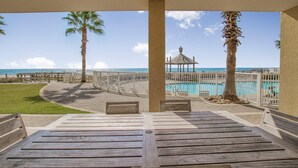 A wooden deck with benches overlooking a pool and beach, with palm trees and a gazebo in the background. - Summer House 103a (Orange Beach)