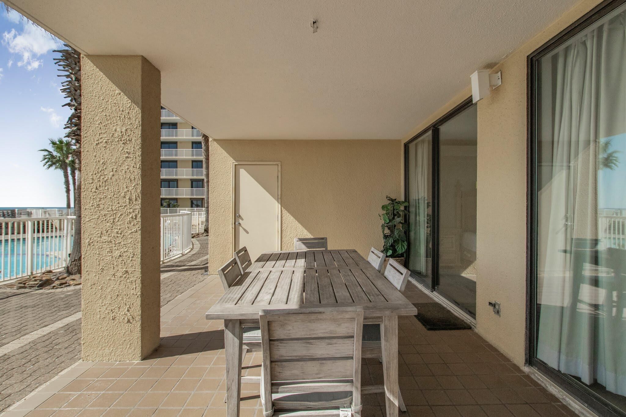 Une table et des chaises en bois sur un balcon donnant sur une piscine et des palmiers.