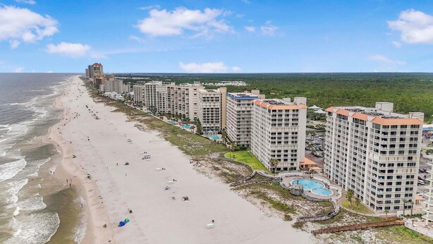 A coastal hotel with multiple high-rise buildings, a sandy beach, and a pool area. - Summer House 103a (Orange Beach)