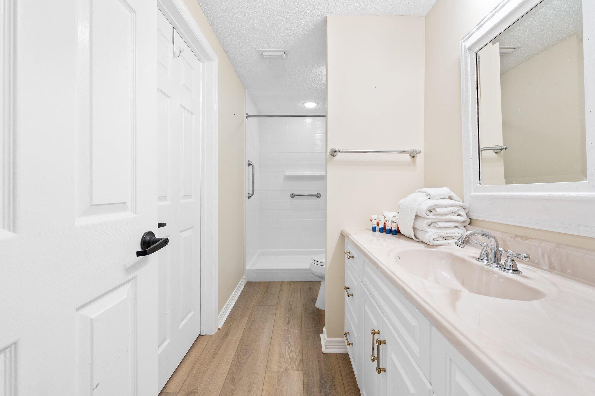 Une salle de bain avec un meuble-lavabo blanc, un évier, un miroir et un espace douche.