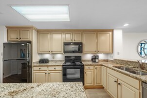 A kitchen with beige cabinets, a stainless steel refrigerator, a microwave, a stove, and a sink.