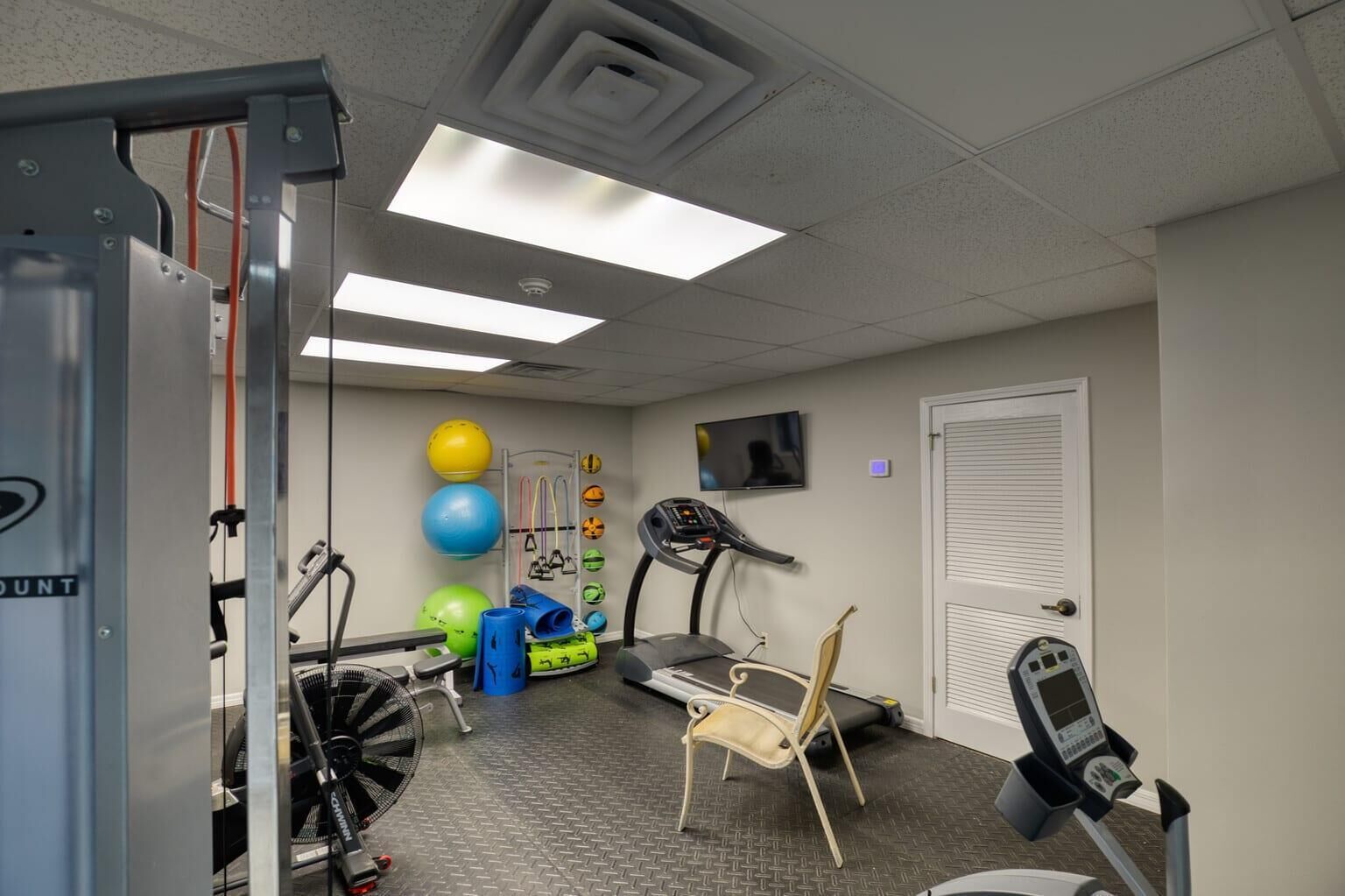 Een fitnessruimte met trainingsapparatuur, een loopband en een televisie aan de muur.