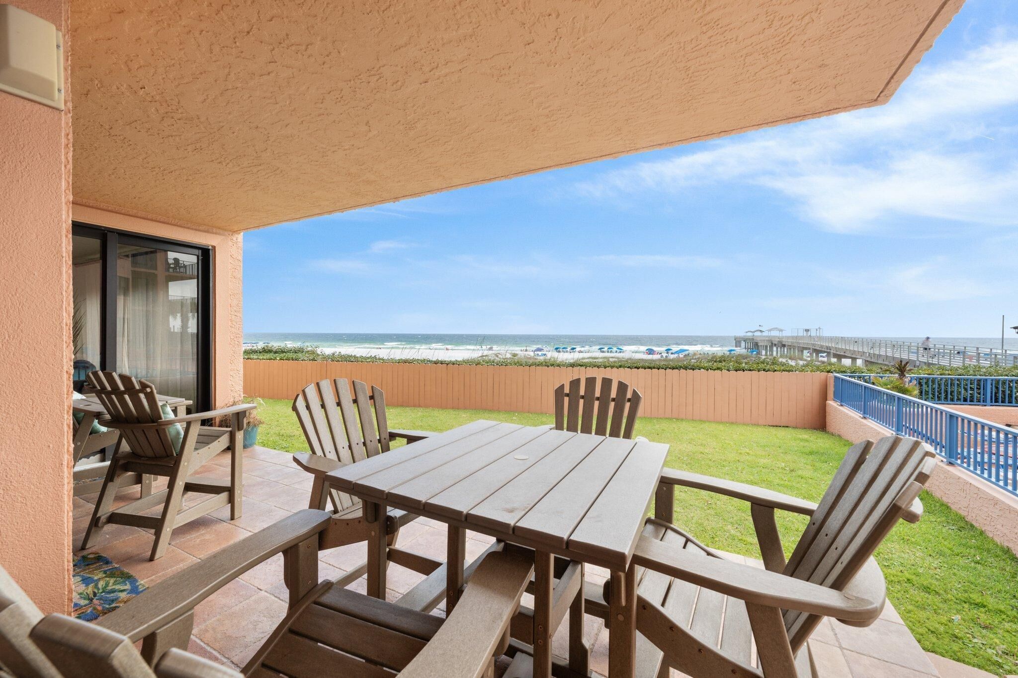 A patio with a wooden table and chairs, overlooking a beach and pier.