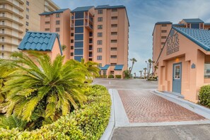 A hotel with a sign reading "FOUR SEASONS" and "MONAR BEACH". It features a paved entrance with palm trees and a clear sky. - Four Seasons 103e (Orange Beach)