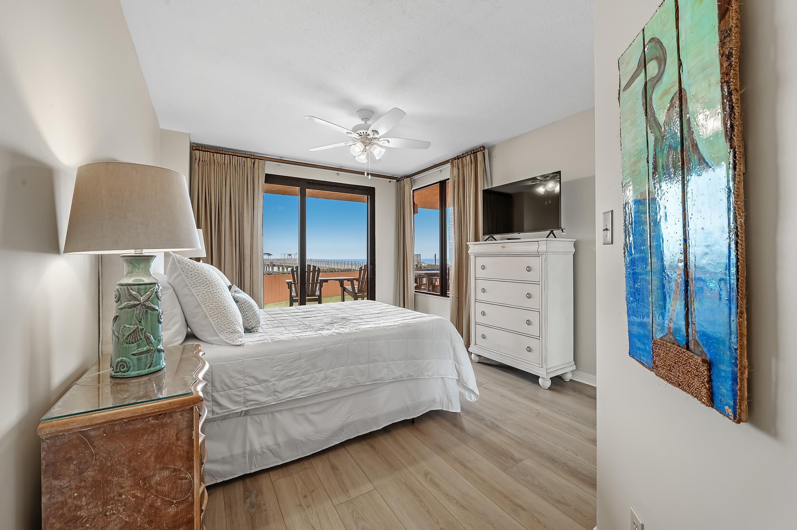 A hotel room with a bed, a ceiling fan, a TV, a dresser, and a painting.