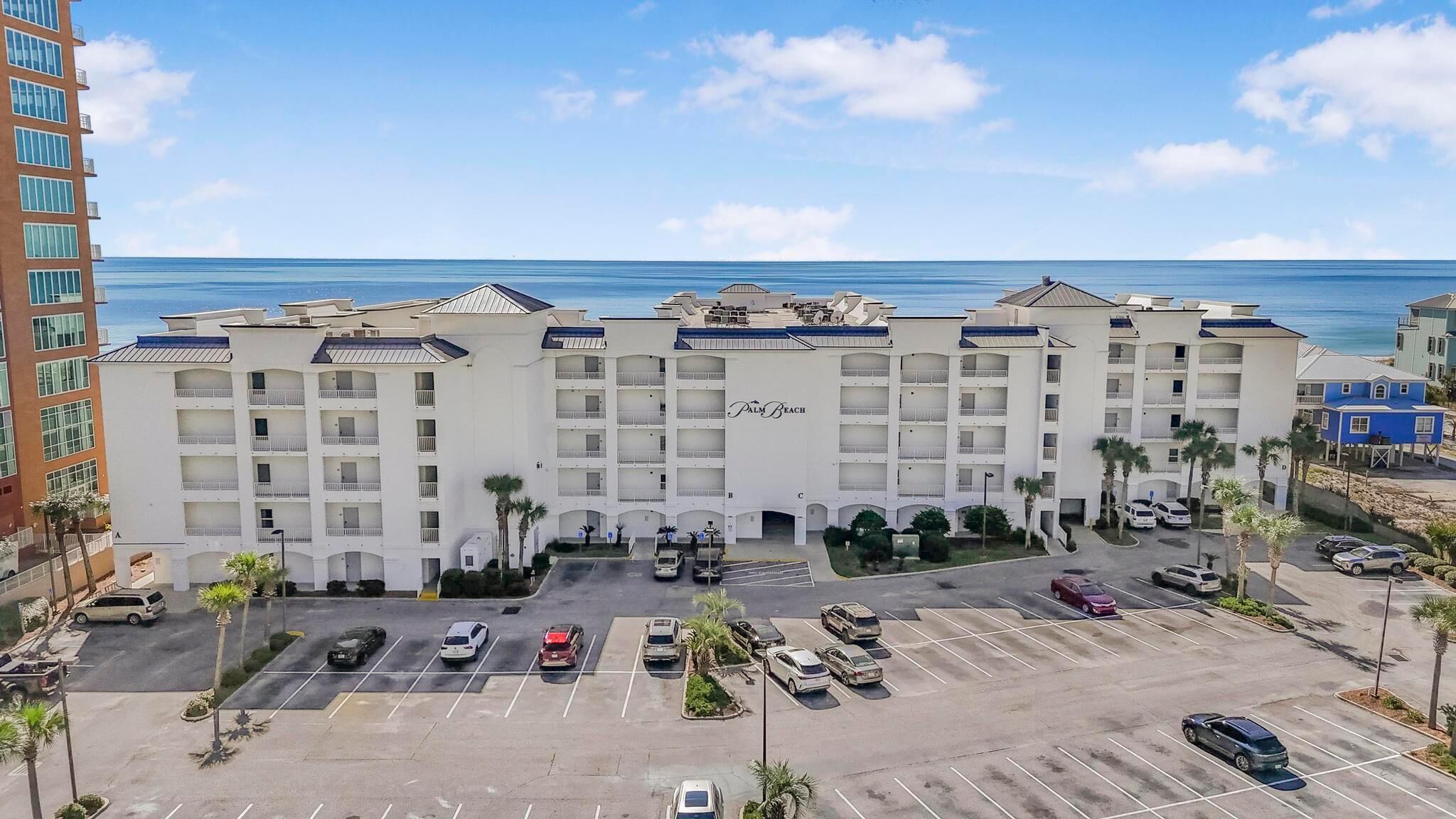 A multi-story hotel with a central courtyard, parking lot, and a view of the ocean.