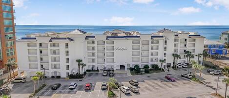 A multi-story hotel with a central courtyard, parking lot, and a view of the ocean.